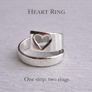Op de afbeelding: Zilveren hartring met een hartvormige uitsparing. De ring is gemaakt van een enkele metalen strip, met de tekst "Heart Ring" en "One strip: two rings" in de afbeelding.