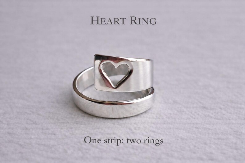 Op de afbeelding: Zilveren hartring met een hartvormige uitsparing. De ring is gemaakt van een enkele metalen strip, met de tekst "Heart Ring" en "One strip: two rings" in de afbeelding.