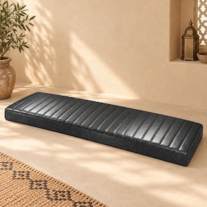 May include: A long, rectangular floor cushion upholstered in black faux leather. The cushion features a series of parallel, vertical stitched channels running across its entire length, creating a uniform, ribbed texture on the top surface.