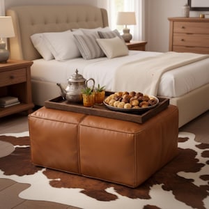 Peut inclure: Scène de chambre avec un ottoman en cuir marron, un plateau en bois avec une théière, des verres et des pâtisseries. Le lit a des draps et des oreillers blancs. Un tapis en peau de vache est au sol.