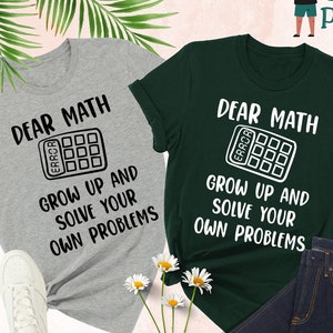 May include: Two t-shirts with the text "Dear Math, Grow Up and Solve Your Own Problems" and a calculator graphic. The shirts are in grey and forest green.