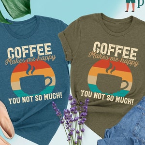 May include: Two t-shirts with a vintage-style graphic of a coffee cup and the text "Coffee Makes Me Happy You Not So Much!" One shirt is heather deep teal and the other is heather olive.