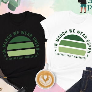 May include: Two t-shirts, one black and one white, with a green sunset graphic and the text "In March We Wear Green & Cerebral Palsy Awareness".