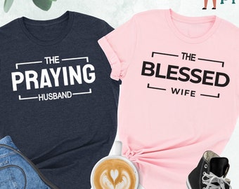 May include: Two t-shirts, one heather navy blue and one pink, with a matching couple's design. The navy blue shirt says "The Praying Husband" and the pink shirt says "The Blessed Wife".