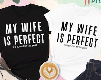 May include: Two black and white t-shirts with the text "My wife is perfect. She bought me this shirt."  The shirts are laid out on a pink and white background.