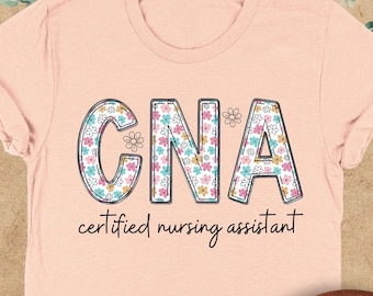 May include: A heather peach t-shirt with a floral design that spells out "CNA" and the text "certified nursing assistant".
