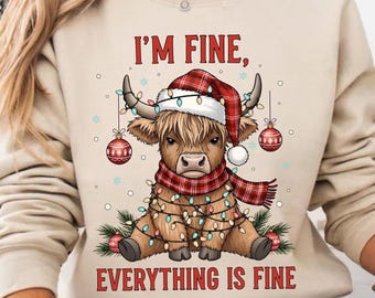 May include: Beige sweatshirt with a festive design featuring a Highland cow wearing a Santa hat and scarf, adorned with Christmas lights and ornaments. The text "I'M FINE, EVERYTHING IS FINE" is printed below the cow.