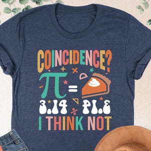 May include: A navy blue t-shirt with a colorful graphic that says "COINCIDENCE? π = 3.14 PIE I THINK NOT".