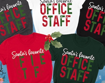 May include: A collection of short-sleeved t-shirts in various colors, including dark grey, white, black, red, and forest green. Each shirt features the text "Santa's favorite OFFICE STAFF" in a festive design, perfect for holiday celebrations.