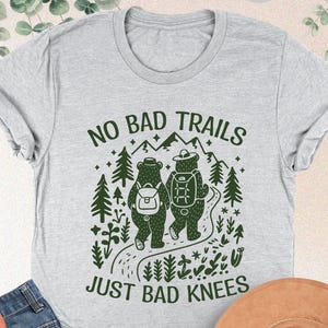 May include: Gray t-shirt with a green graphic of two bears hiking on a trail with the text "No Bad Trails Just Bad Knees".