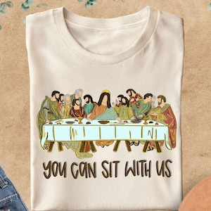 May include: A white t-shirt with a vintage illustration of Jesus and his disciples at the Last Supper. The text "You can sit with us" is printed below the image.