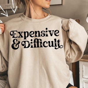 May include: A beige sweatshirt with the text "Expensive & Difficult" in black retro-style lettering.