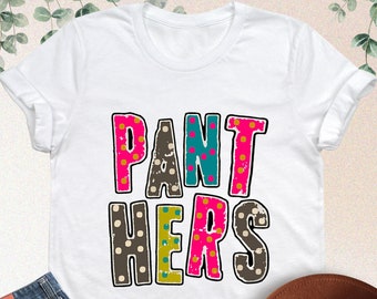 May include: White t-shirt with the words "PANT HER'S" in colorful, patterned letters. The letters are in a distressed, vintage style.