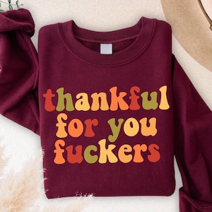 May include: Maroon sweatshirt with the text "thankful for you fuckers" in orange, yellow, and green. The sweatshirt is folded with the sleeves cuffed. The word "MAROON" is in a circle in the upper right corner.