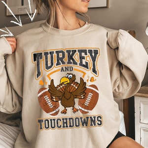 May include: A beige sweatshirt with a vintage-style graphic of a turkey and footballs. The text reads "TURKEY AND TOUCHDOWNS".