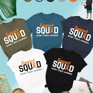 May include: Five t-shirts in different colors with the text "Support Squad" and an orange ribbon printed on the front. The text "#Kidney Cancer Awareness" is printed below the ribbon. The t-shirts are displayed on a light blue background.