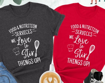 May include: Two t-shirts with the text "Food & Nutrition Services - We Love to Stir Things Up!" printed on them. One shirt is dark heather grey and the other is red.