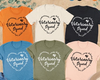 May include: Six different color t-shirts with the text "Compassionate, Caring, Dedicated, Veterinary Squad" in a heart shape with a paw print inside the heart. The text is in black and the heart is in white.