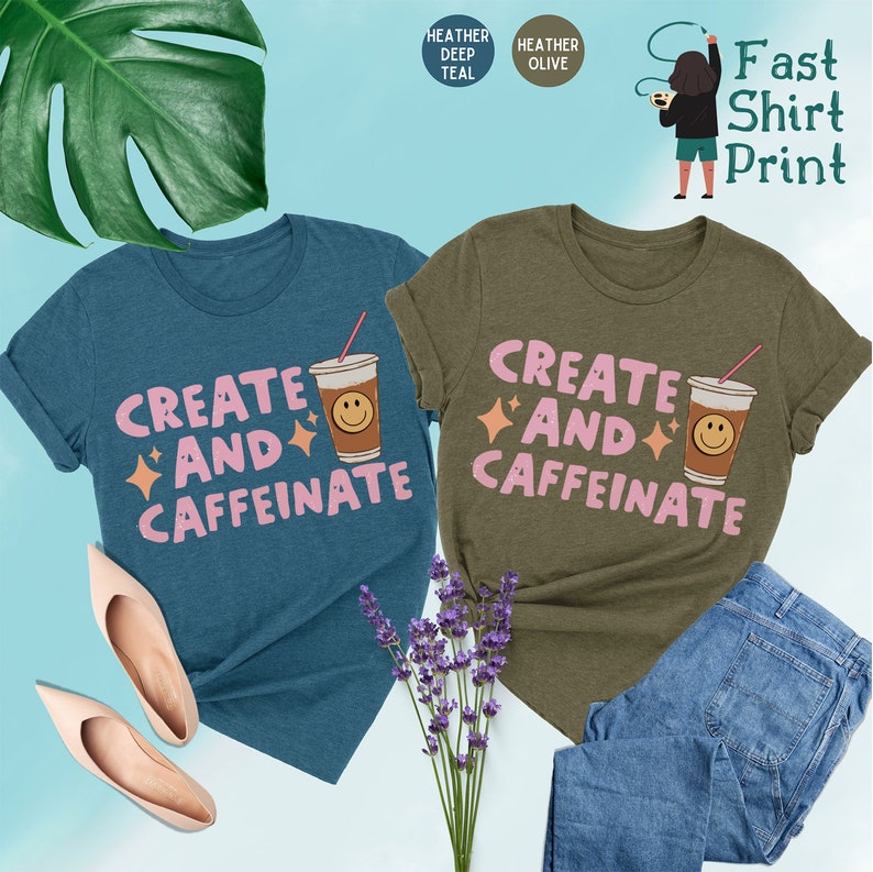 May include: Two t-shirts with a coffee cup graphic and the text "Create and Caffeinate" in pink. The shirt on the left is heather deep teal and the shirt on the right is heather olive.