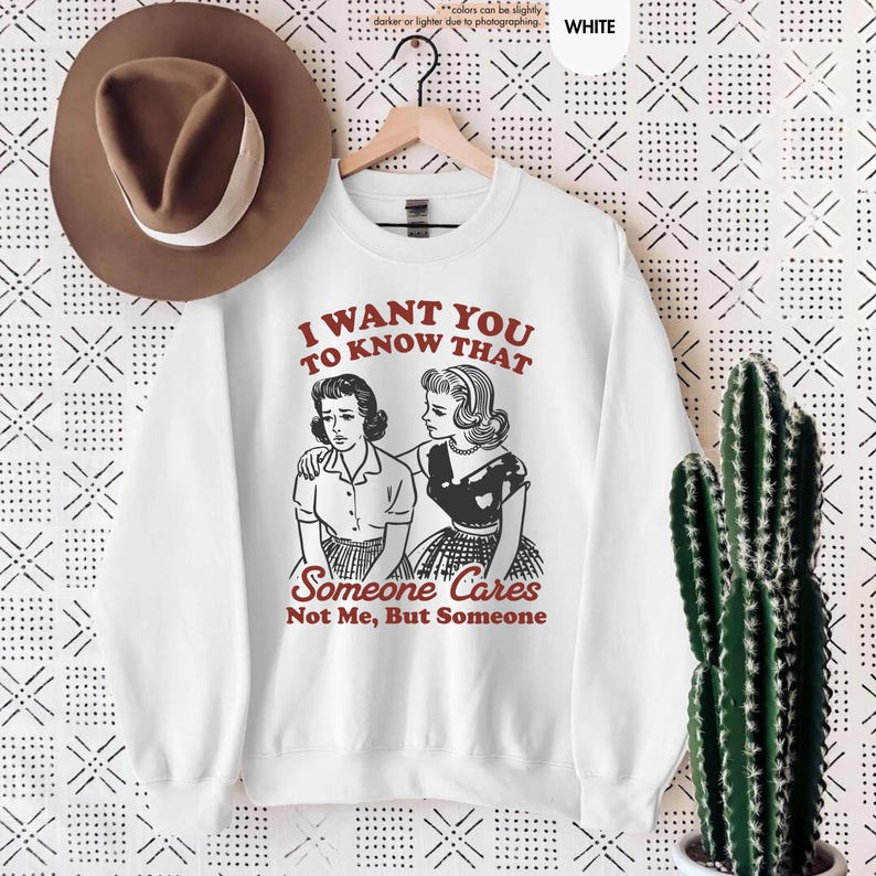 May include: White sweatshirt with the text "I WANT YOU TO KNOW THAT Someone Cares Not Me, But Someone" in red. The graphic features a vintage illustration of two women. A brown hat hangs above the sweatshirt.