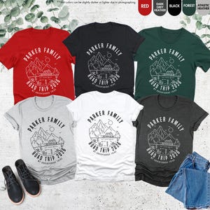 May include: Several short-sleeved t-shirts in colours like red, black, and grey. Each shirt displays a mountain and lake graphic with the text "PARKER FAMILY ROAD TRIP 2026". The shirts are made of a soft material.
