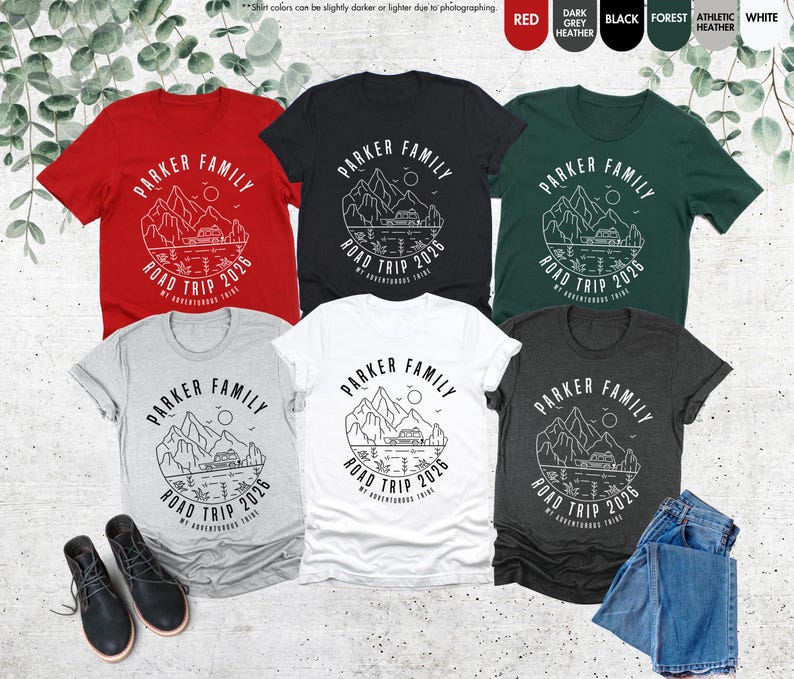 May include: Several short-sleeved t-shirts in colours like red, black, and grey. Each shirt displays a mountain and lake graphic with the text "PARKER FAMILY ROAD TRIP 2026". The shirts are made of a soft material.