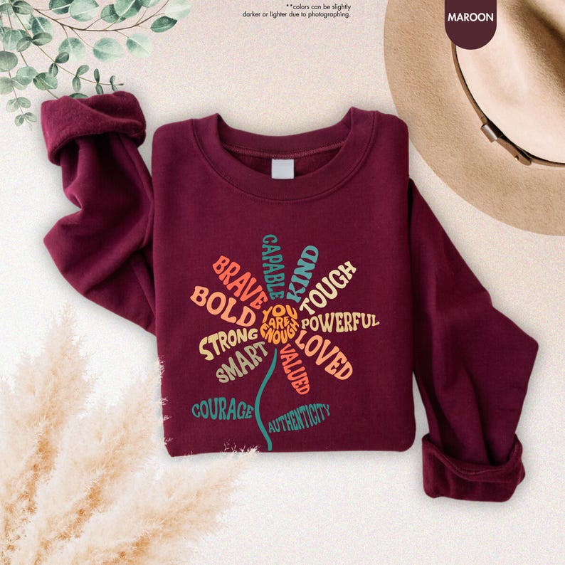 Pode incluir: Camisola bord&ocirc; com um design floral com palavras como "Corajoso", "Forte" e "Gentil". A parte superior de manga comprida tem gola redonda e punhos enrolados. O texto "You are enough" est&aacute; no centro do design floral.