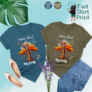 May include: Two t-shirts with a Native American design. The design features a tree with feathers and the text "Native Blood runs through my veins". The t-shirts are available in heather deep teal and heather olive.