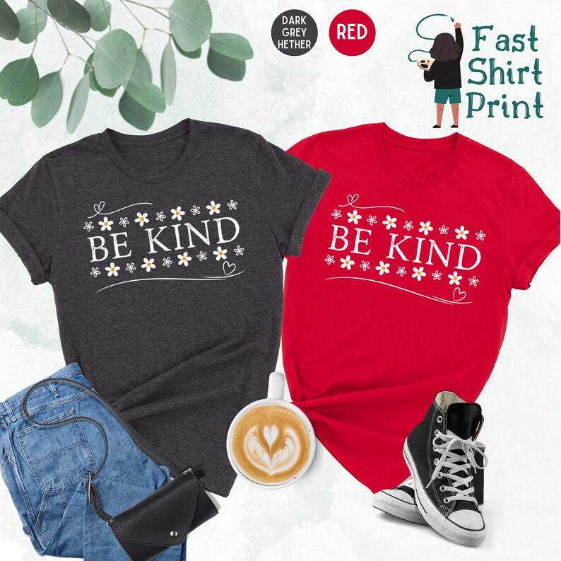 K&ouml;nnte beinhalten: Zwei T-Shirts mit dem Text "Be Kind" in wei&szlig;en Buchstaben, umgeben von kleinen wei&szlig;en Blumen. Die Shirts sind in dunkelgrau meliert und rot.