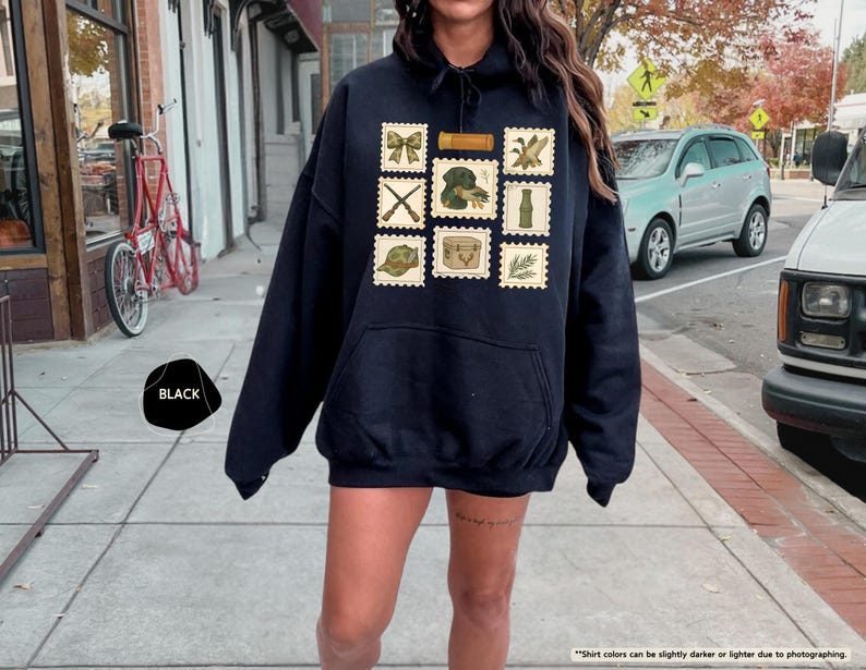 K&ouml;nnte beinhalten: Schwarzer Kapuzenpullover mit Fronttasche und rechteckigem Patch-Design. Der Patch zeigt Briefmarken-Illustrationen von Schleife, gekreuzten Gewehren, Hund, Flasche, Hut, Kiste und Blattzweig. Das Wort "BLACK" ist ebenfalls sichtbar.