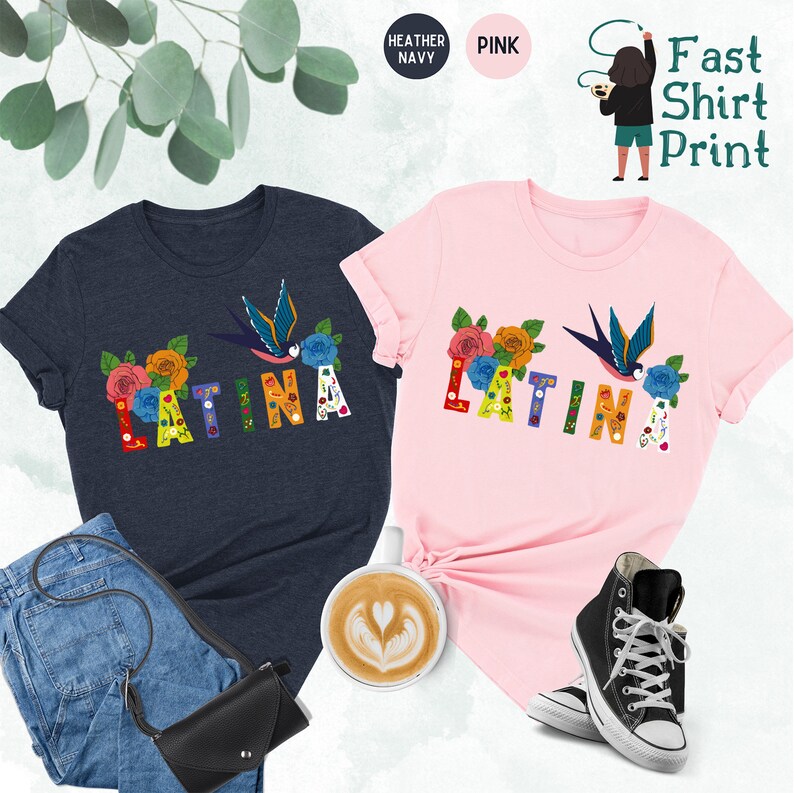 May include: Two t-shirts with the word "LATINA" printed in colorful letters with floral and bird designs. The shirts are available in heather navy and pink.