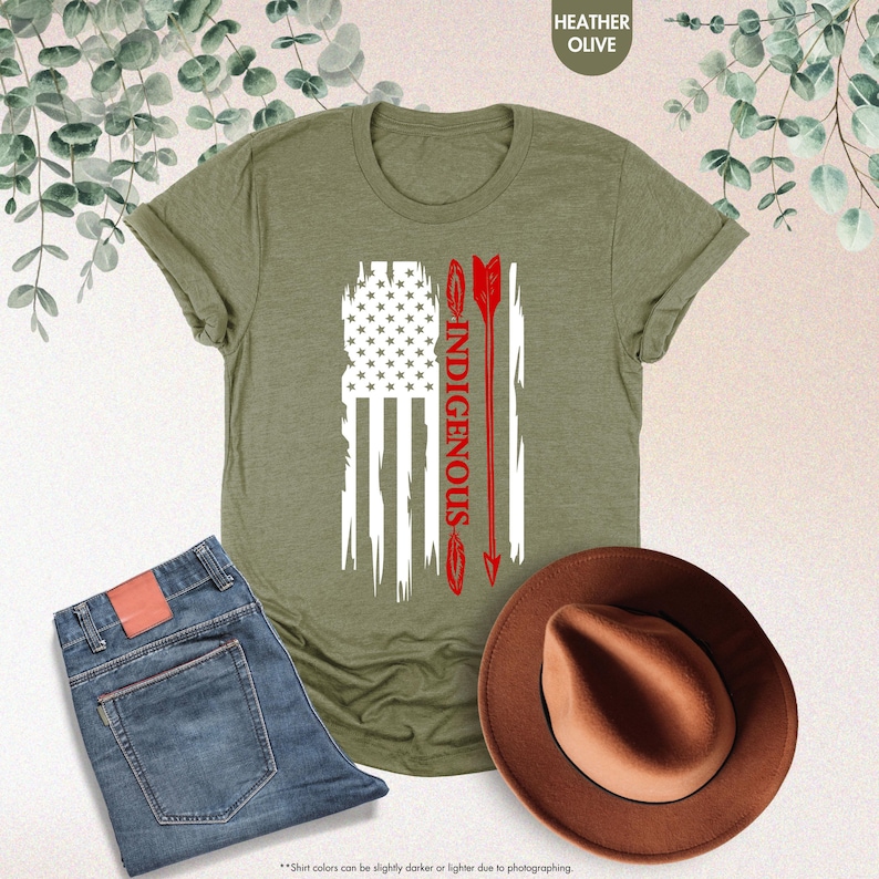 May include: A green t-shirt with a white and red American flag design. The flag is distressed and has an arrow with the word "INDIGENOUS" written on it.