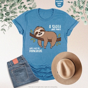 K&ouml;nnte beinhalten: Ein tief tealfarbenes T-Shirt mit einem Faultier-Motiv auf einem Ast und dem Text "A sloth does more work than my pancreas". Das Bild zeigt auch eine blaue Jeans und einen beigen Hut.