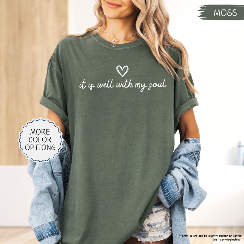 K&ouml;nnte beinhalten: Ein moosgr&uuml;nes T-Shirt mit hochgekrempelten &Auml;rmeln. Das Shirt hat den Schriftzug "it is well with my soul" in wei&szlig;er Schrift und ein kleines Herzsymbol. Die Worte "More Color Options" stehen in einem wei&szlig;en Kreis.