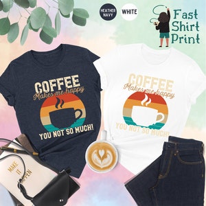 May include: Two t-shirts with a vintage-style coffee cup graphic and the text "Coffee Makes Me Happy You Not So Much!" printed on them. The shirts are in heather navy and white.