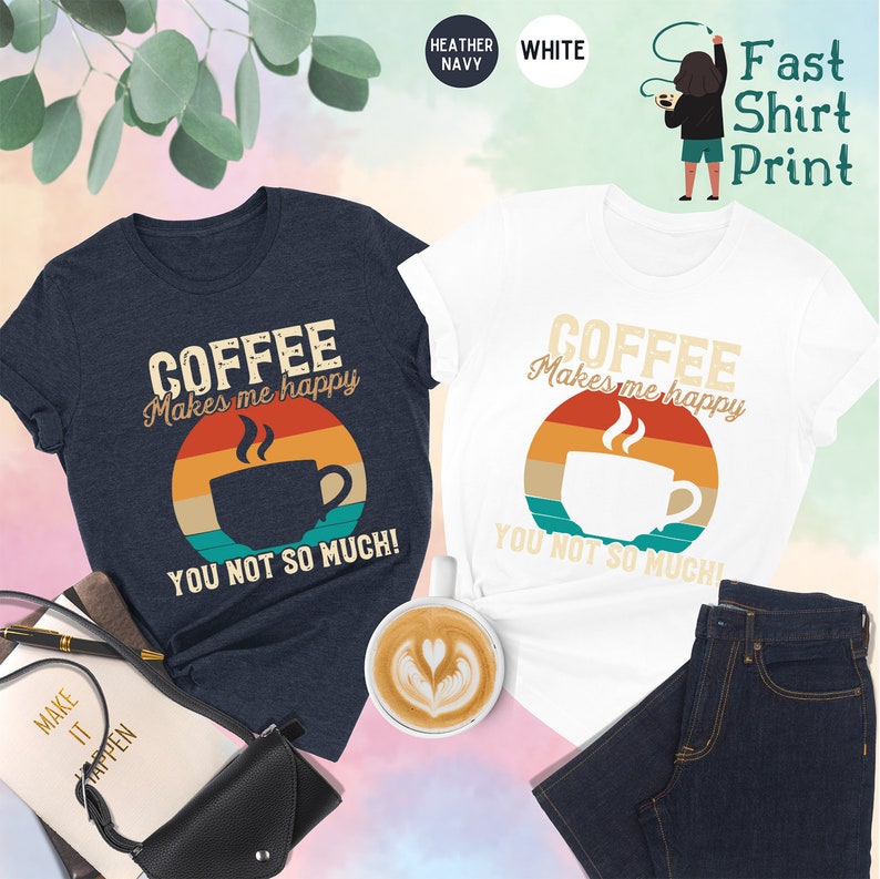 May include: Two t-shirts with a vintage-style coffee cup graphic and the text "Coffee Makes Me Happy You Not So Much!" printed on them. The shirts are in heather navy and white.