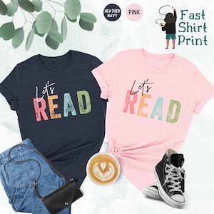 May include: Two t-shirts with the text "Let's Read" in colorful, distressed letters. The shirts are in heather navy and pink.