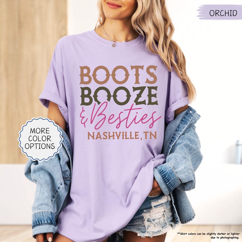 Pu&ograve; includere: Una maglietta lilla con la scritta "BOOTS BOOZE & Besties" in marrone, verde oliva e rosa, con "NASHVILLE, TN" sotto. La maglietta fa parte di una collezione di abbigliamento.