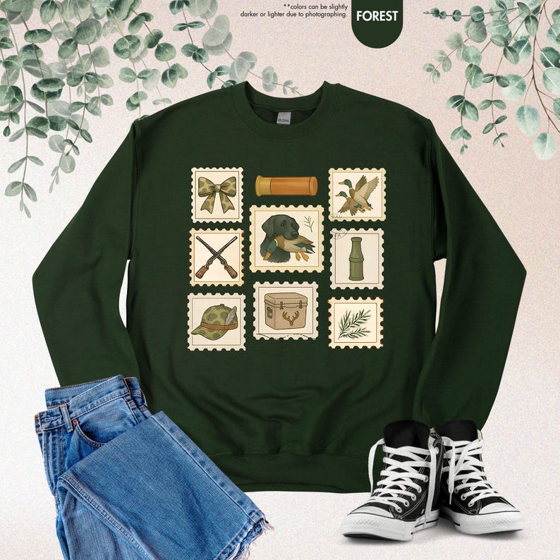 K&ouml;nnte beinhalten: Forstgr&uuml;nes Sweatshirt mit Jagd-Postwertzeichen-Designs. Die Briefmarken zeigen eine Schleife, einen Hund mit Ente, gekreuzte Gewehre, einen Jagdhut, eine Jagdtasche und andere jagdbezogene Illustrationen.