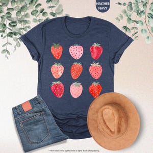 May include: A navy blue t-shirt with a repeating pattern of red and pink strawberries. The shirt is made of a soft, comfortable material.