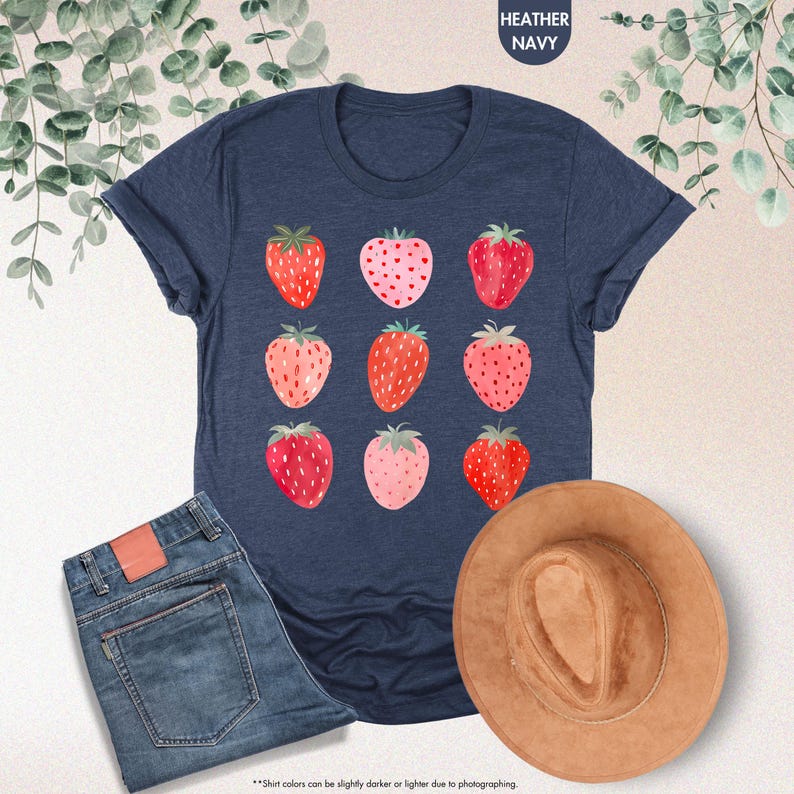 May include: A navy blue t-shirt with a repeating pattern of red and pink strawberries. The shirt is made of a soft, comfortable material.