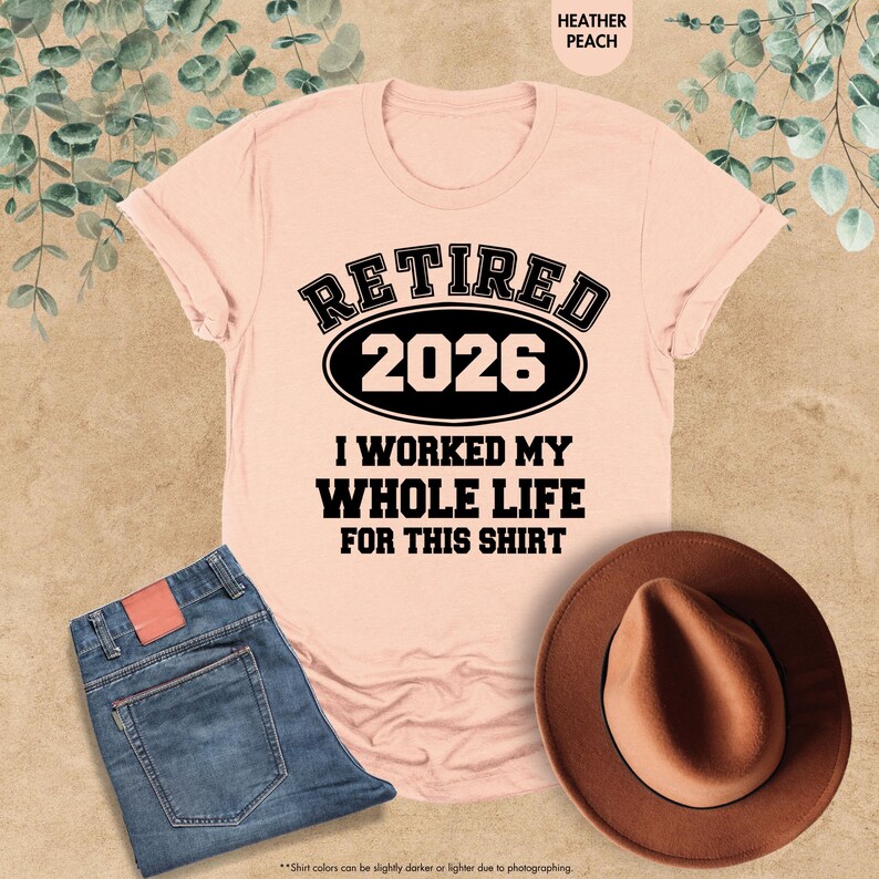 Puede incluir: Una camiseta color melocot&oacute;n con el texto "RETIRED 2026 I WORKED MY WHOLE LIFE FOR THIS SHIRT" en negro. La imagen tambi&eacute;n incluye unos vaqueros azules y un sombrero marr&oacute;n.