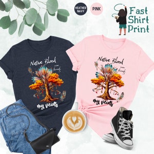 May include: Two t-shirts with a Native American design. The design features a tree with feathers and the text "Native Blood runs through my veins". The shirts are available in heather navy and pink.