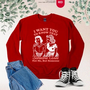 May include: A red sweatshirt with the text "I WANT YOU TO KNOW THAT Someone Cares Not Me, But Someone" in white. The graphic depicts two women. The sweatshirt is paired with blue jeans and black and white sneakers.
