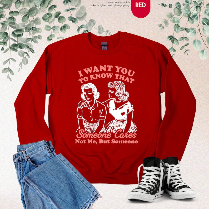 May include: A red sweatshirt with the text "I WANT YOU TO KNOW THAT Someone Cares Not Me, But Someone" in white. The graphic depicts two women. The sweatshirt is paired with blue jeans and black and white sneakers.