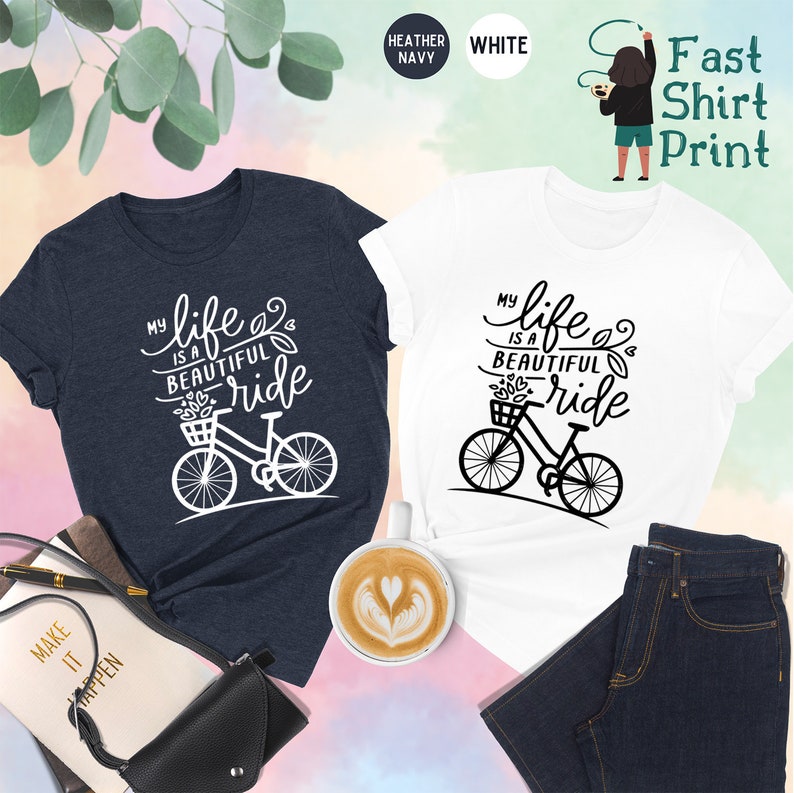 May include: Two t-shirts with a bicycle graphic and the text "My life is a beautiful ride". The shirts are available in heather navy and white.