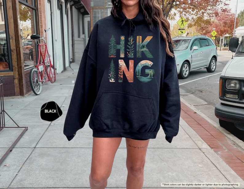 Pode incluir: Camisola de moletom com capuz preta com uma estampa gr&aacute;fica da palavra "HIKING" com cenas da natureza incorporadas nas letras.
