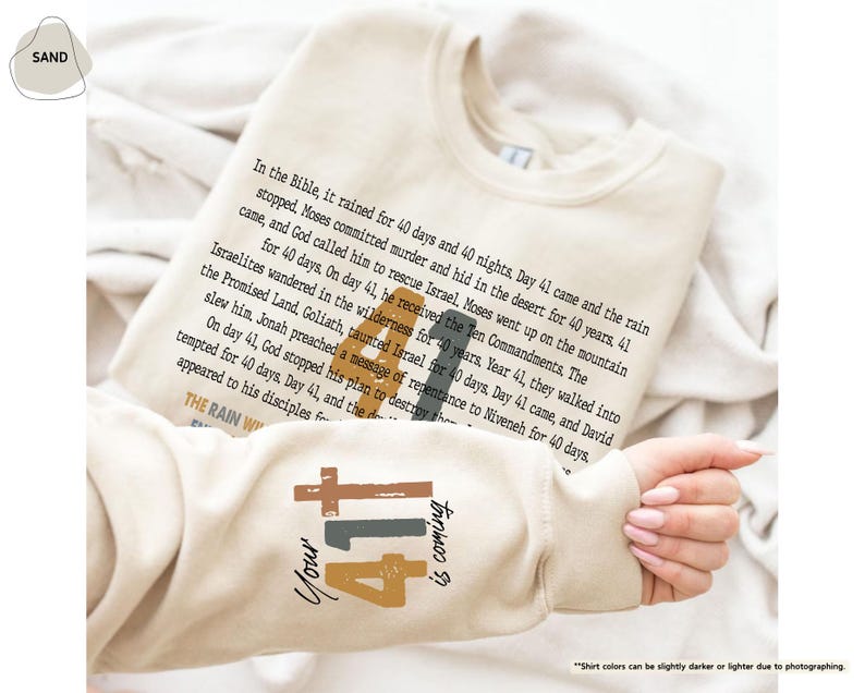May include: A beige sweatshirt with a brown and black graphic design featuring the number 41 and the text "Your 41 is coming". The text "In the Bible, it rained for 40 days and 40 nights, Day 41 came and the rain stopped, Moses committed murder and hid in the desert for 40 years, 41 came, and God called him to rescue Israel, Moses went up on the mountain for 40 days. On day 41, he received the Ten Commandments, The Israelites wandered in the wilderness for 40 years, Year 41, they walked into the Promised Land, Goliath, taunted Israel for 40 days, Day 41 came, and David slew him, Jonah preached a message of repentance to Niveneh for 40 days. On day 41, God stopped his plan to destroy the tempted for 40 days. Day 41, and the appeared to his disciples for the THE RAIN W" is printed on the sweatshirt.