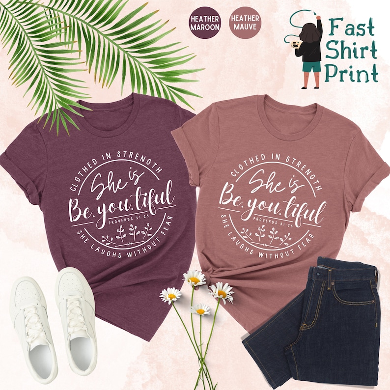 May include: Two heather t-shirts, one maroon and one mauve, with the text "She is Be.you.tiful" in a circular design. The shirts are paired with white sneakers and dark blue jeans. The words "Fast Shirt Print" are also visible.