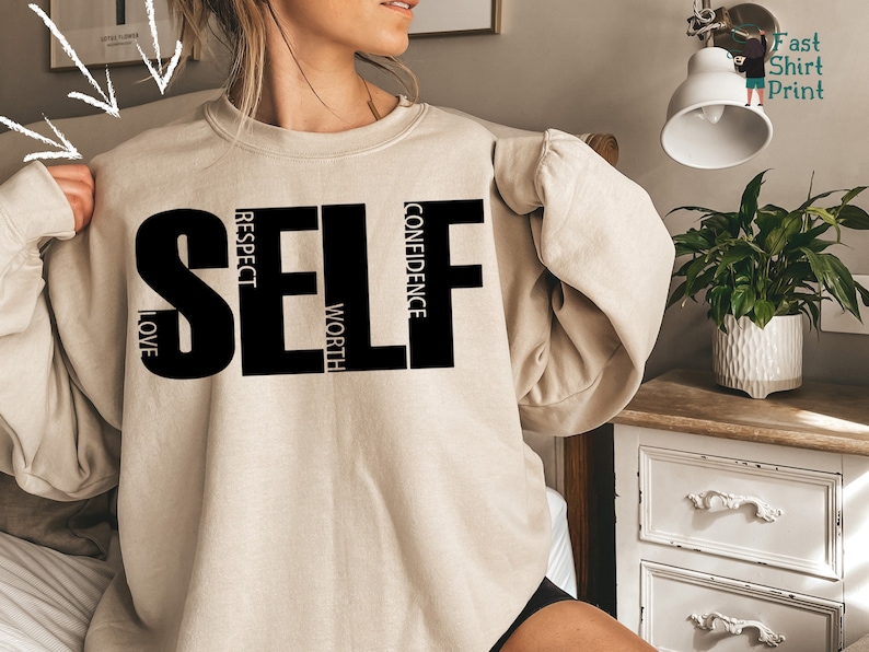 May include: A beige sweatshirt with the word "SELF" printed in black. The letters are made up of the words "love", "respect", "worth", and "confidence".
